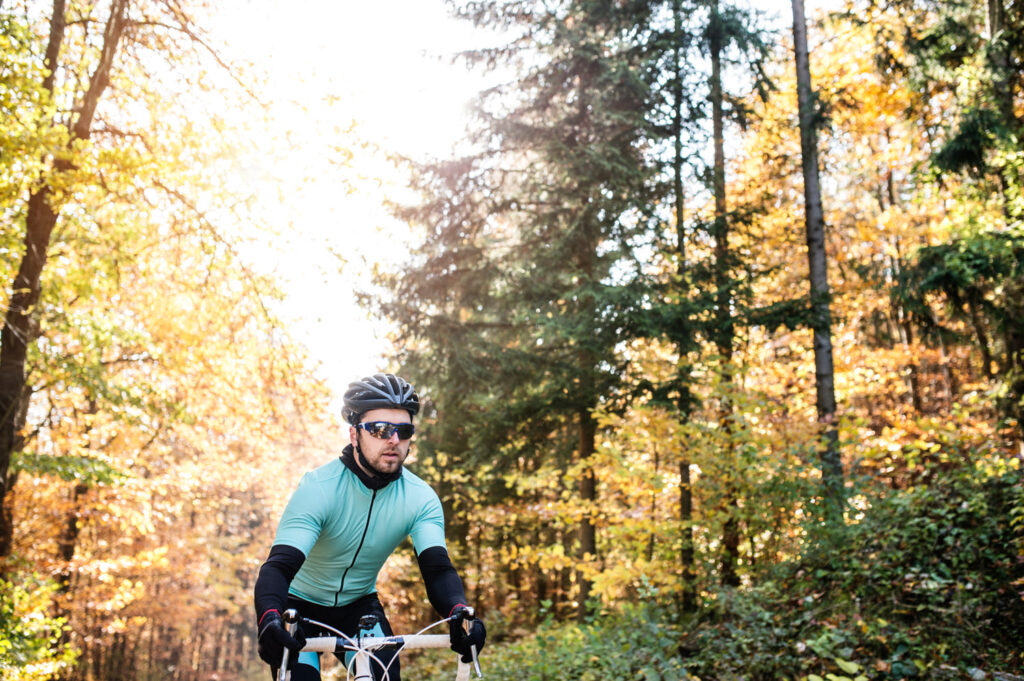 Young sportsman riding bicycle outside in sunny autumn nature with cycling sunglasses